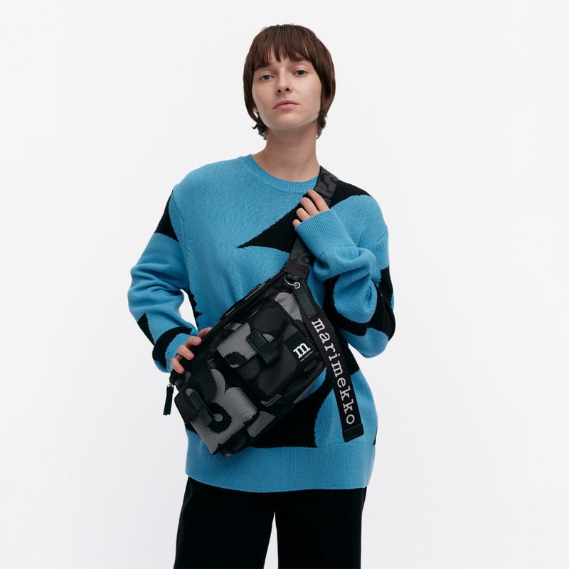 Person wearing a blue sweater holding a black waist bag with &