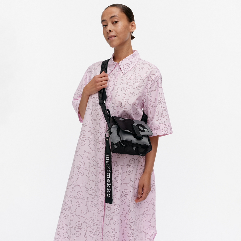 Woman wearing a pink floral dress with a black and gray patterned bag on a white background