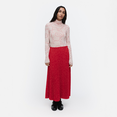 Woman wearing a patterned top and red pleated skirt on a white background