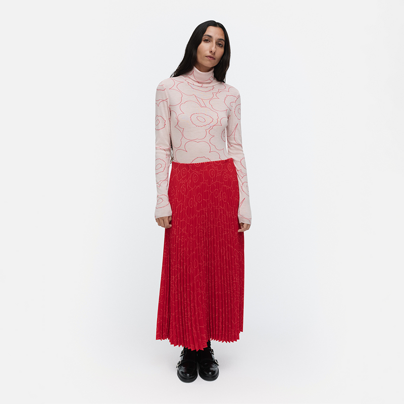 Woman wearing a patterned top and red pleated skirt on a white background