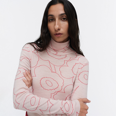 Woman wearing a light pink turtleneck with red floral patterns on a white background