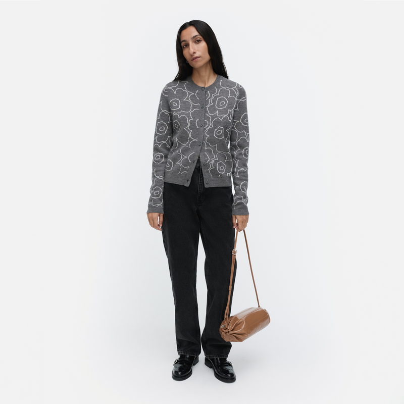Person wearing a patterned gray sweater and black pants, holding a brown bag on a white background