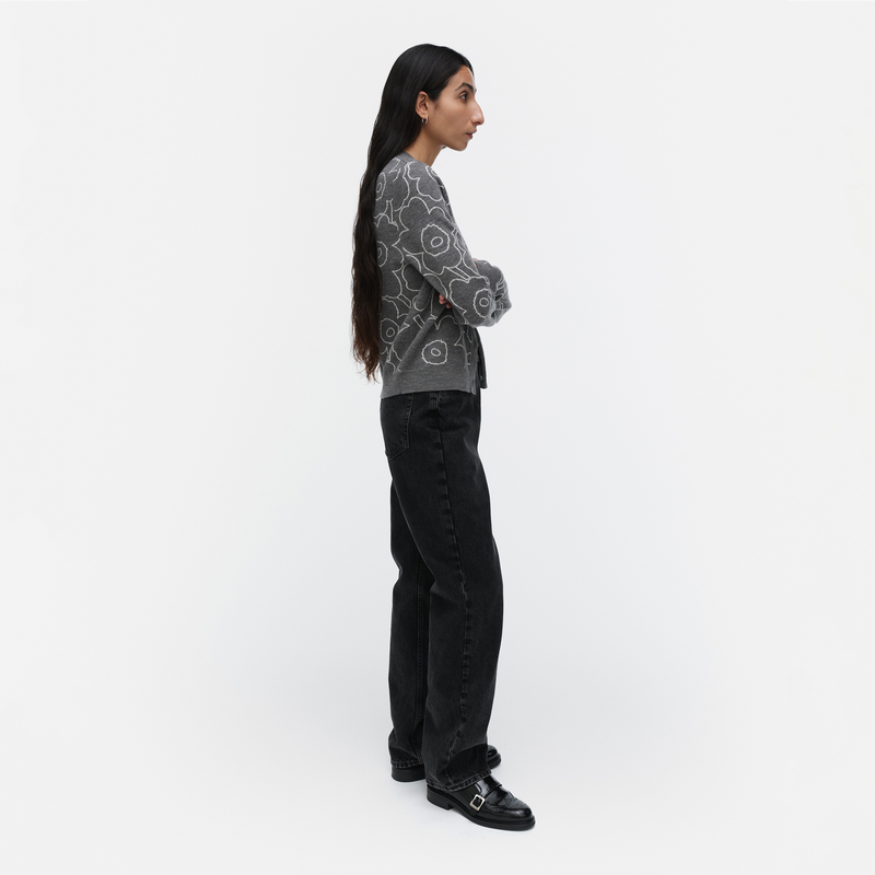 Person wearing a patterned sweater and black pants on a white background