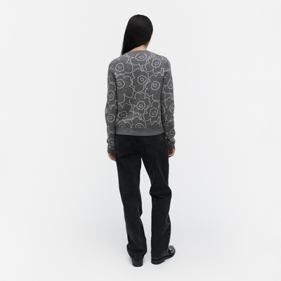 Person wearing a patterned gray sweater and black pants on a white background