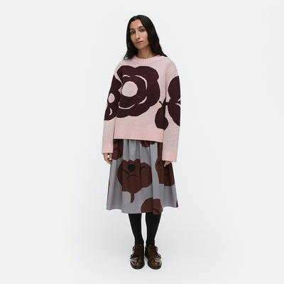 Woman wearing a pink sweater with brown floral patterns and a matching skirt on a white background