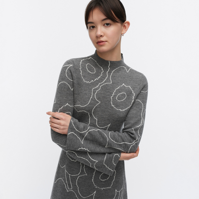 Woman wearing a gray sweater with white floral patterns on a light gray background