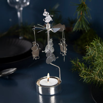 Decorative candle holder with snowman design on a dark surface with a blurred background