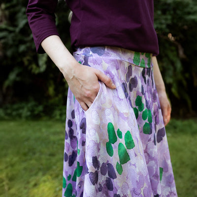 Person wearing a purple floral skirt with green leaves in an outdoor setting