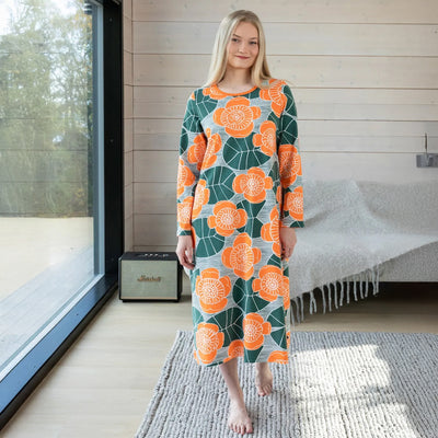 Woman wearing a floral dress standing in a modern room with a window and bed in the background.