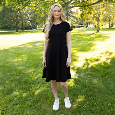 Woman in a black dress standing on grass with trees in the background
