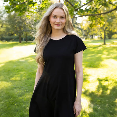 Woman in a black dress standing in a park with green grass and trees.