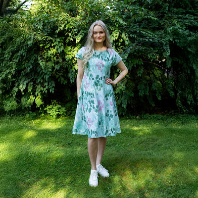 Woman in a floral dress standing in a grassy area with greenery
