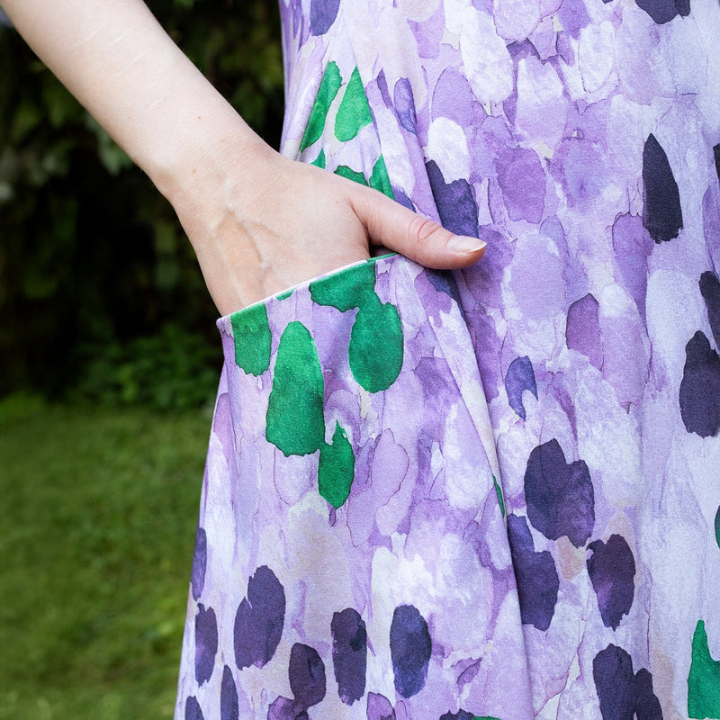 Person wearing a purple dress with green and black leaf patterns, standing outdoors.