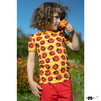 Child enjoying field of flowers in ladybug shirt