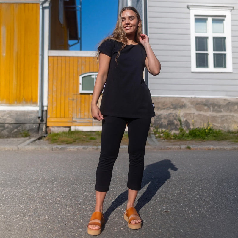 Woman in black outfit standing on a street with a colorful building in the background