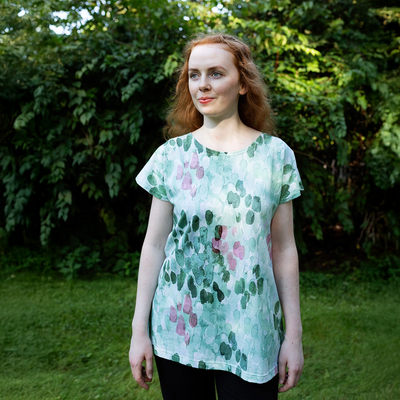 Woman wearing a green floral patterned shirt standing outdoors with greenery in the background