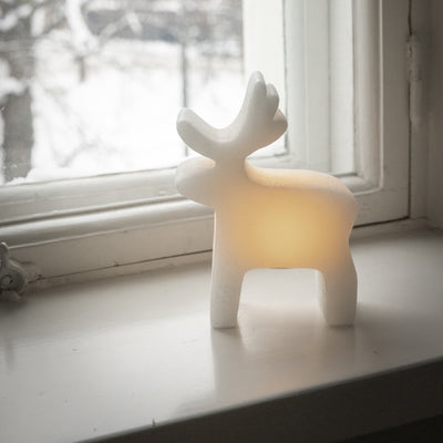 White deer-shaped lamp on a windowsill with a snowy outdoor view.