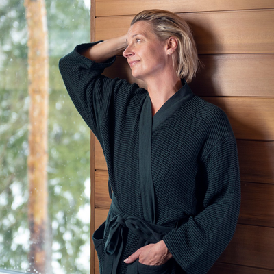Woman wearing robe resting against sauna wall