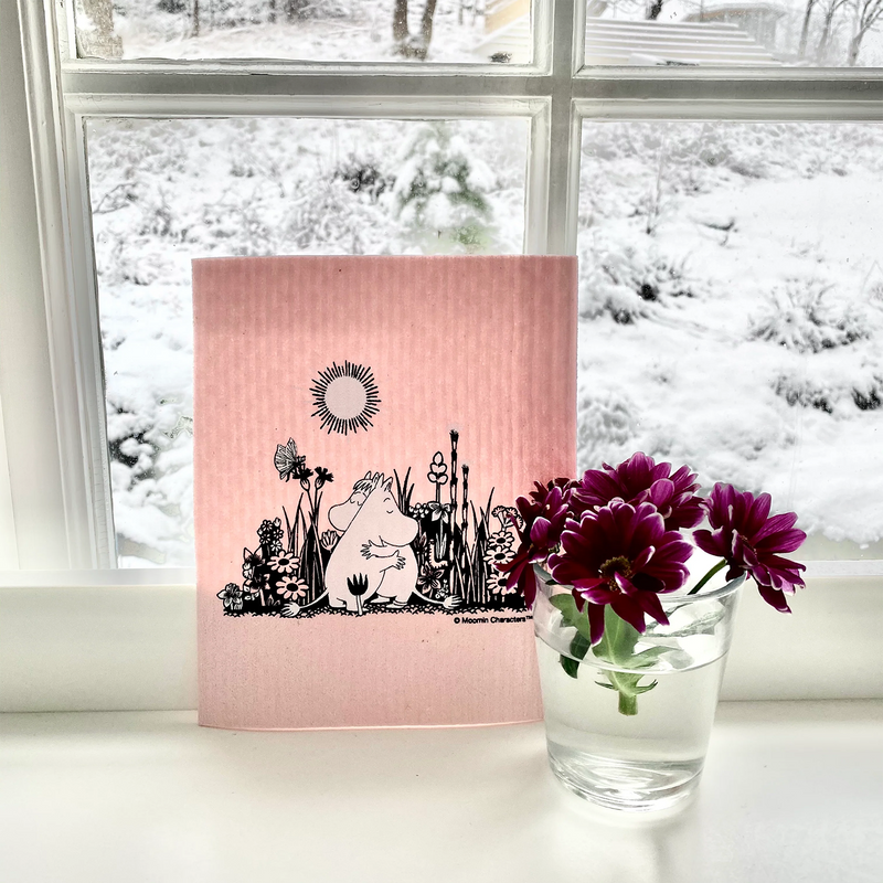Pink dishcloth with black illustration of a character and plants on a windowsill with a snowy view.