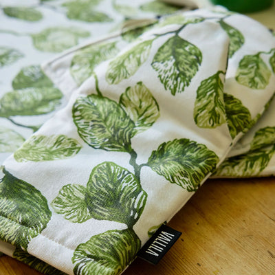 Folded fabric with green leaf pattern on a wooden surface, featuring a visible brand label.