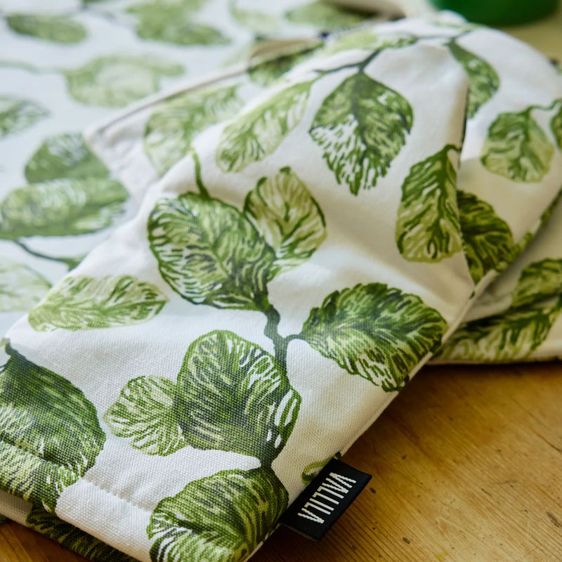 Folded fabric with green leaf pattern on a wooden surface, featuring a visible brand label.