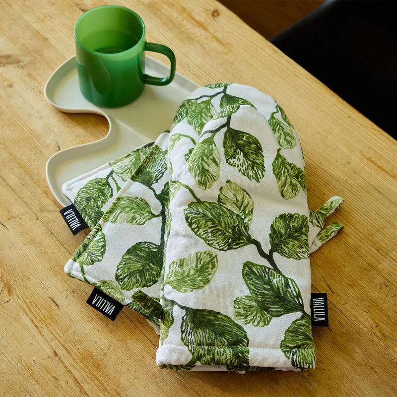 Two green leaf-patterned towels on a wooden surface with a green mug.