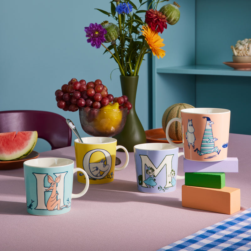 Colorful mugs with letter designs on a table with fruits and flowers.