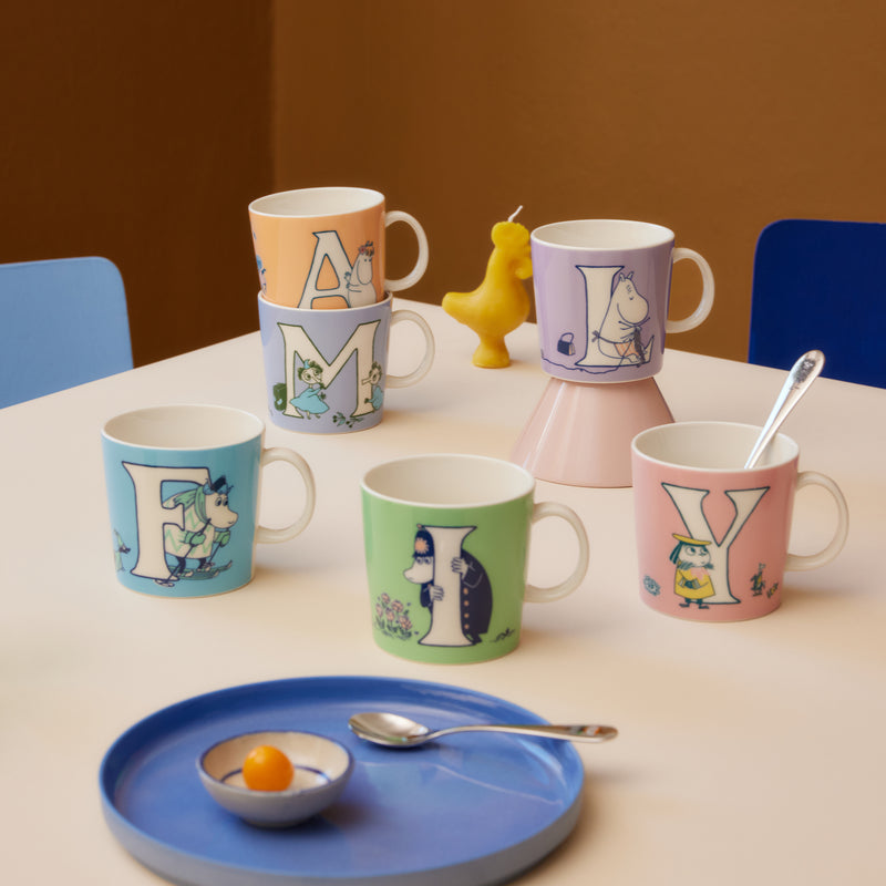 Colorful mugs with cartoon characters on a table with a blue tray and spoon.