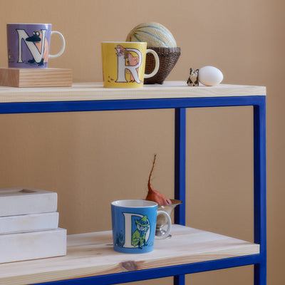 Colorful mugs with letter designs on a wooden shelf against a beige wall.