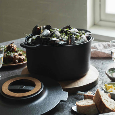 Black pot with green herbs on a table with bread and other dishes