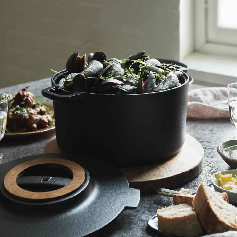 Black pot with green herbs on a table with bread and other dishes