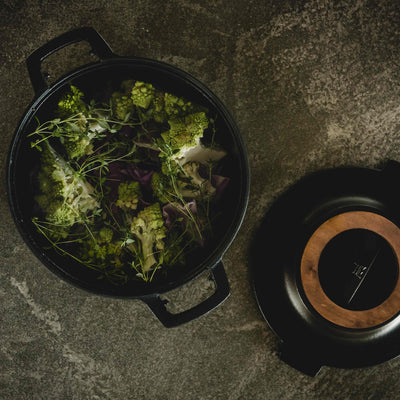 Black cast iron pot with green leafy vegetables on a stone surface