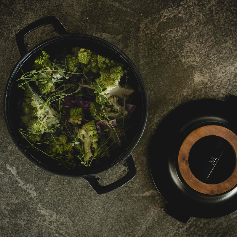 Black cast iron pot with green leafy vegetables on a stone surface