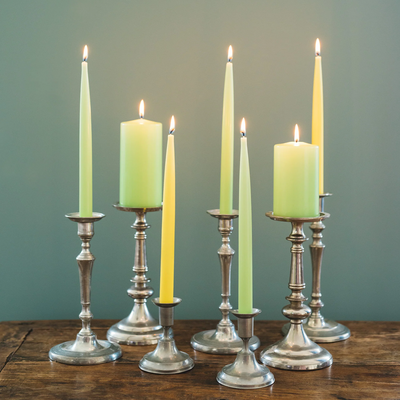 Set of candles in various colors on metallic candlesticks against a green background