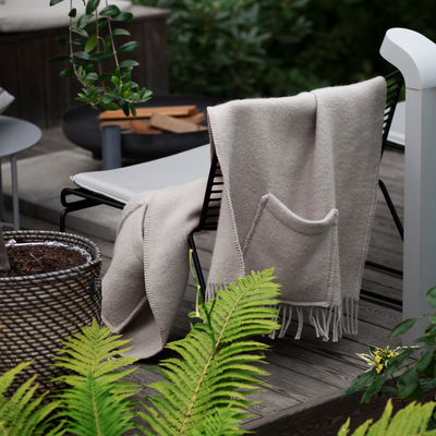 Beige blanket draped over a chair on a wooden deck with plants around