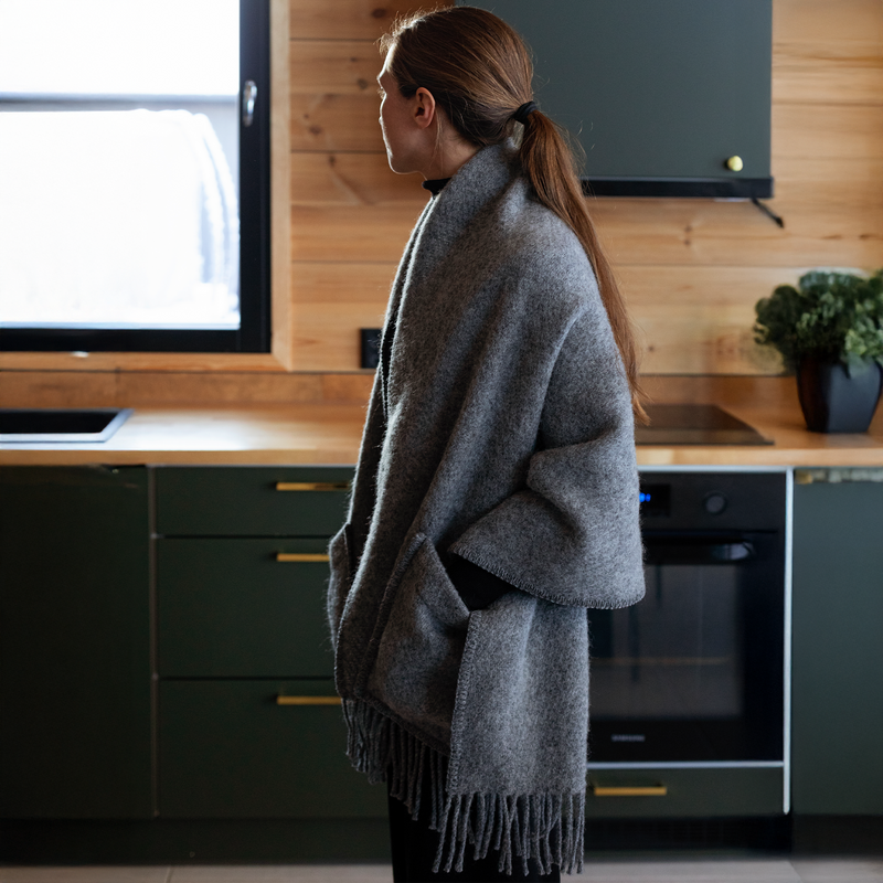 Person wearing a gray coat in a kitchen with wooden cabinets and black appliances.