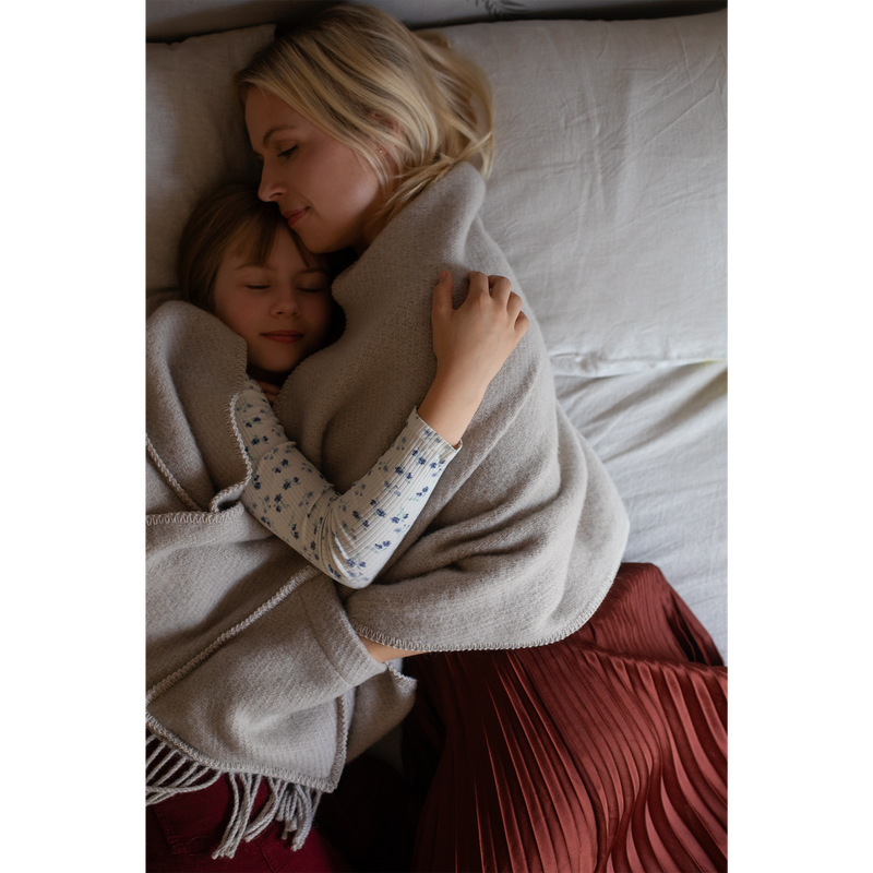 Woman and child hugging under a blanket on a bed