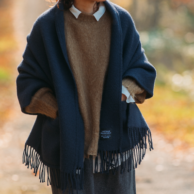 Person wearing a dark blue fringed scarf with a blurred natural background