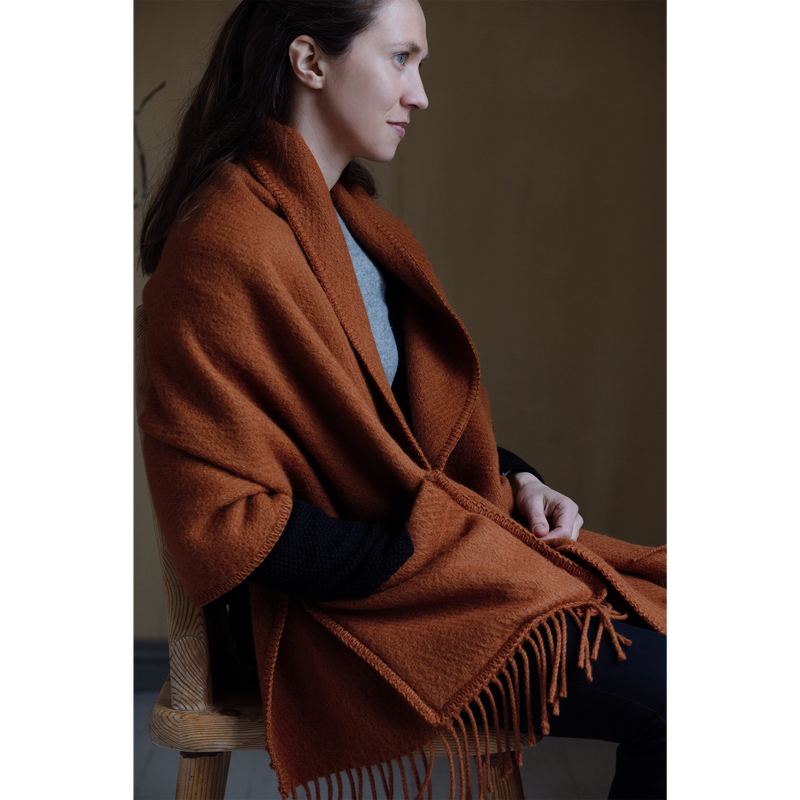 Woman wearing a brown blanket draped over her shoulders, sitting on a chair.