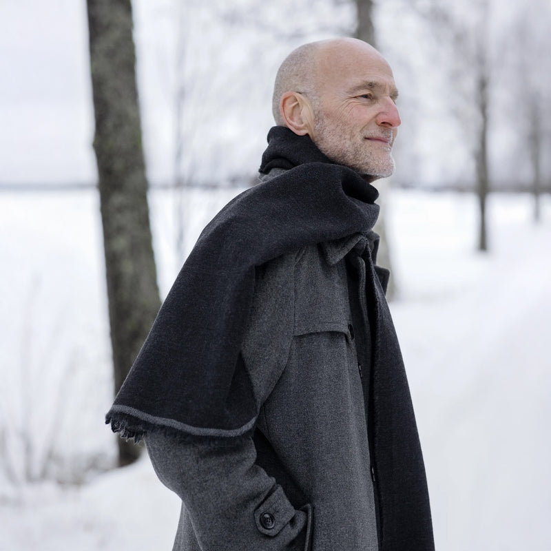 Man wearing a gray coat with a black cape in a snowy landscape