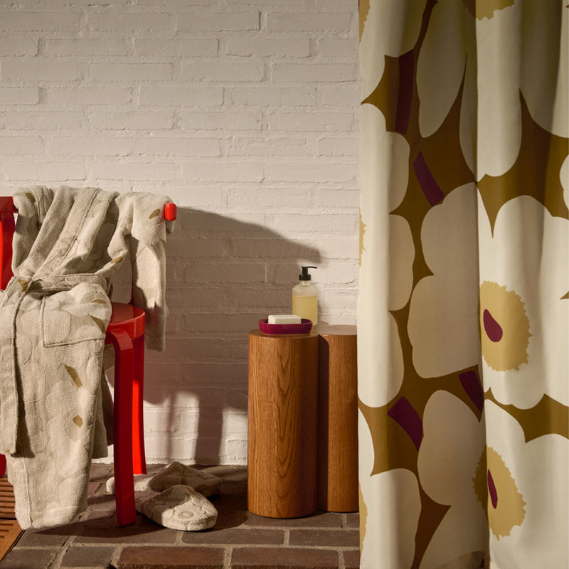 Bathroom with a floral shower curtain, red stool, and white bathrobe.