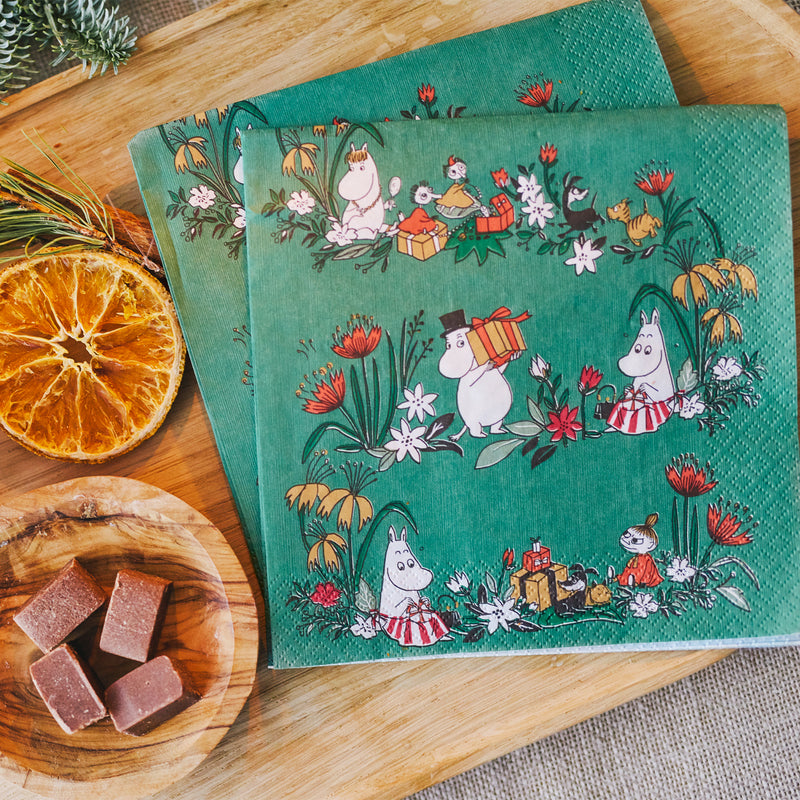 Two green illustrated napkins with characters on a wooden surface with dried oranges and cookies.