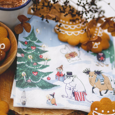 Napkin with Christmas-themed design featuring characters and a tree, surrounded by cookies and a cup.
