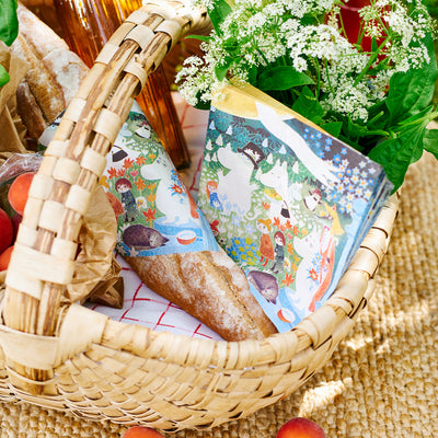 Wicker picnic basket with bread, fruits, and a colorful book on a textured surface.