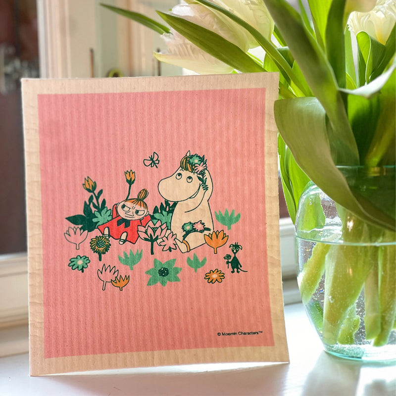 Pink towel with cartoon characters on a wooden surface next to a vase with green plants.