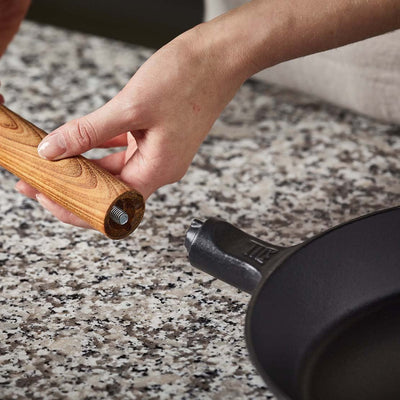Person adjusting a wooden handle on a black frying pan on a speckled countertop