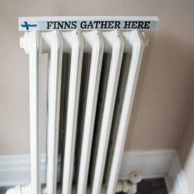 Shelf Sitter Sign Finns Gather Here on top of heating unit