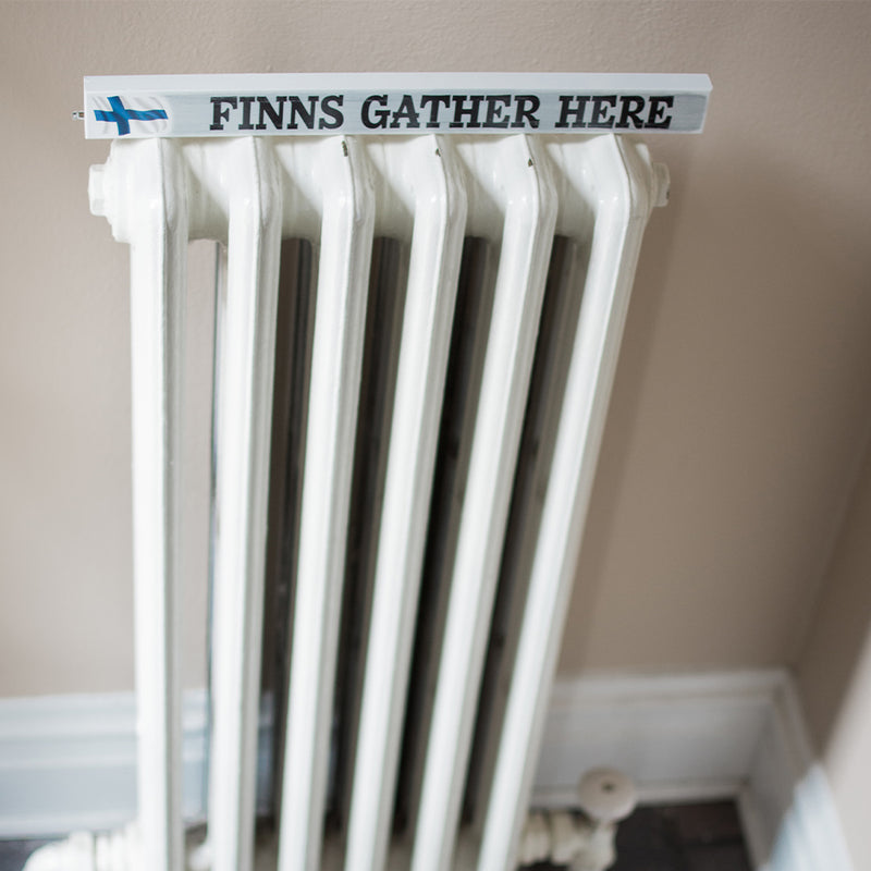 Shelf Sitter Sign Finns Gather Here on top of heating unit