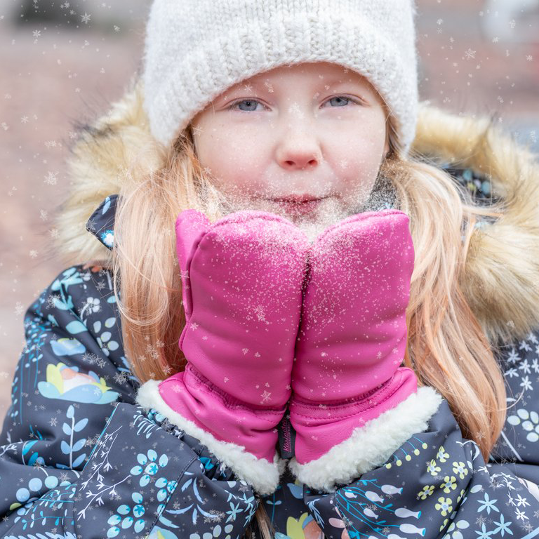 Child blowing snow dust with leather mittens on