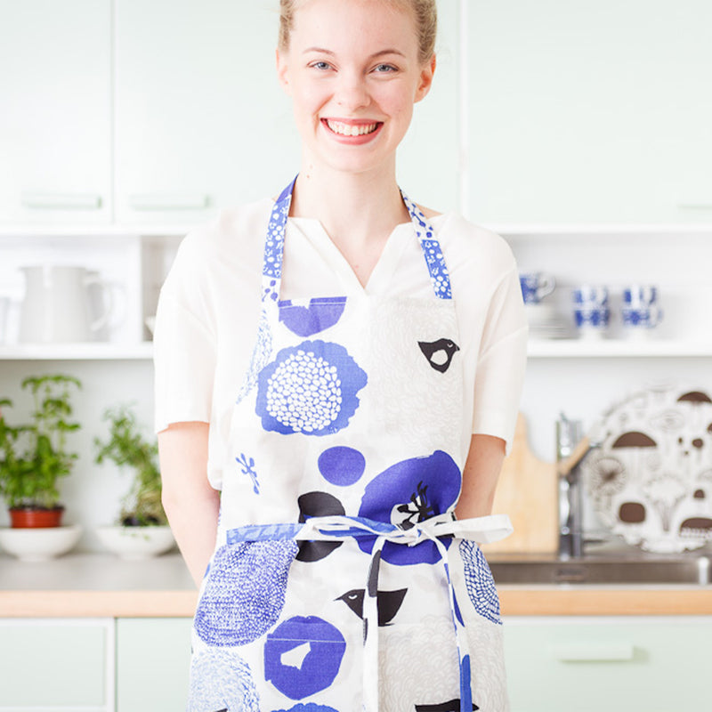 smiling person in white top wearing Sunnuntai Blue Apron